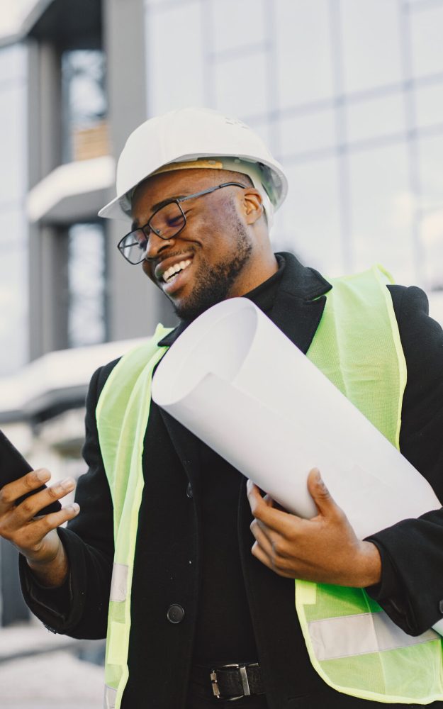 Young black race man with blueprint stading near glass building. Talking by phone.