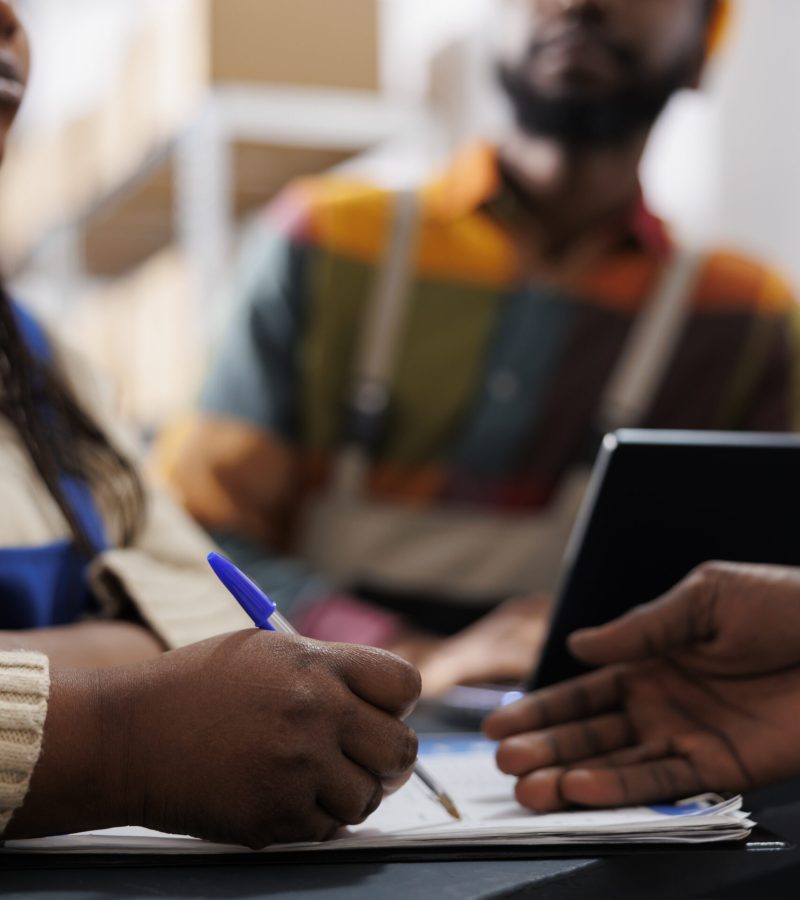 African american woman warehouse worker hand writing in clipboard at reception desk. Storehouse employees checking order list and managing documentation at post office checkout close up
